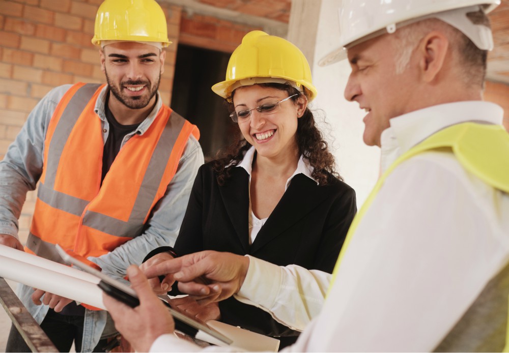 A group of people in hard hats going over construction plans smiling.